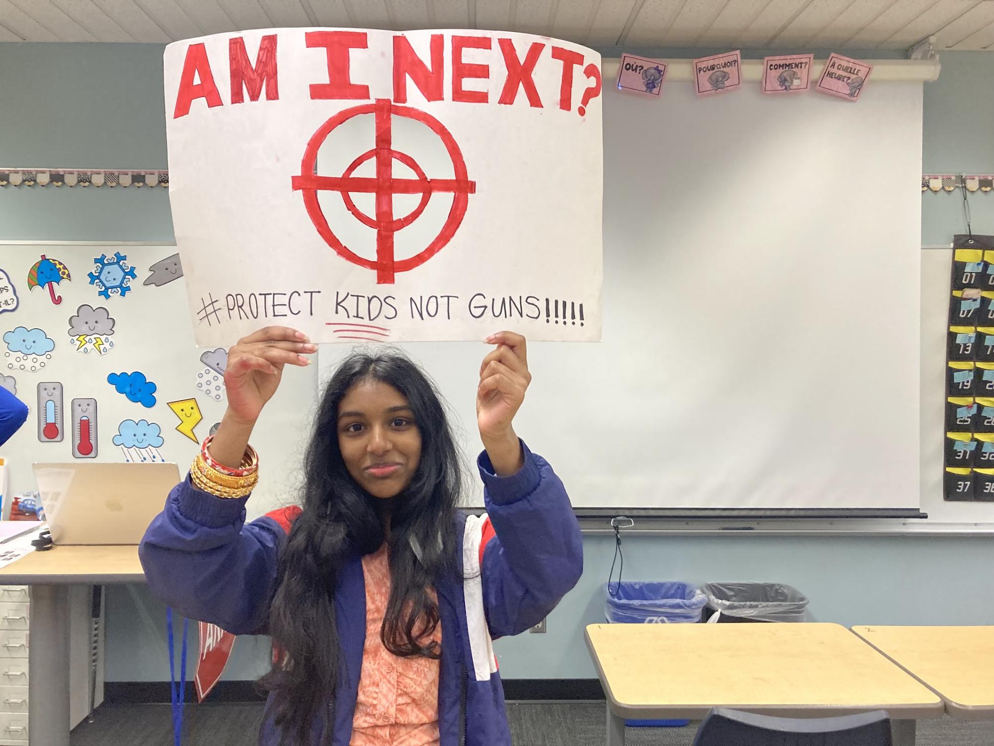 Sophomore Anushka Bosco holds a sign inside a classroom stating, "Am I next? #protect kids not guns!"